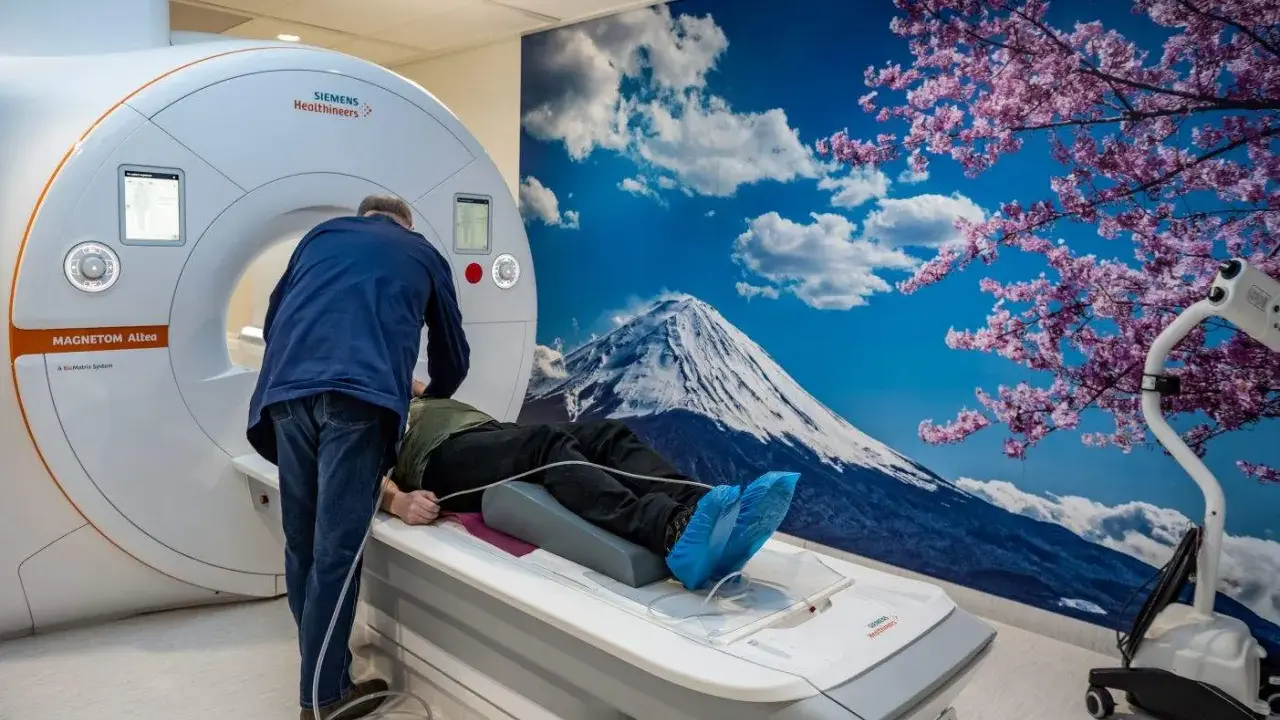 Pacjent leży na łóżku rezonansu magnetycznego, przygotowywany do badania. Za nim ściana z widokiem na górę Fudżi i kwitnącą wiśnię, tworząc silne wzmocnienie kontrastowe.