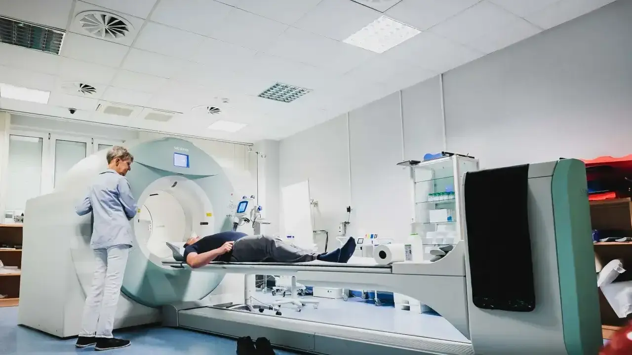 Pacjent leży na stole aparatu do tomografii komputerowej, nadzorowany przez technika.