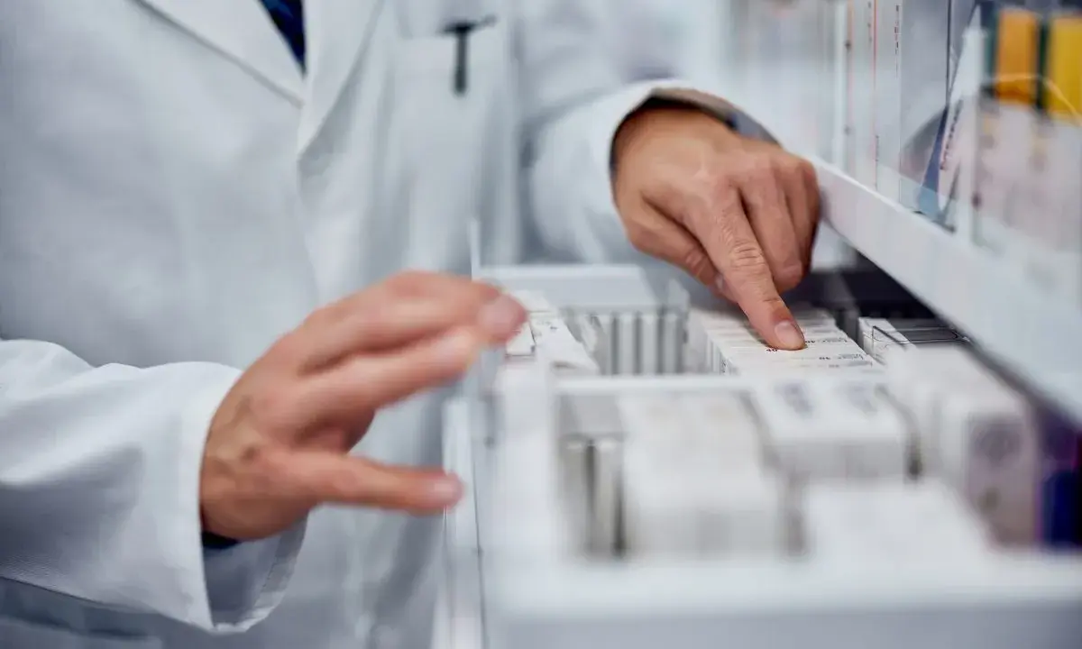 Farmaceuta szuka zamiennika leku Zarixa, przeglądając opakowania leków w aptece.