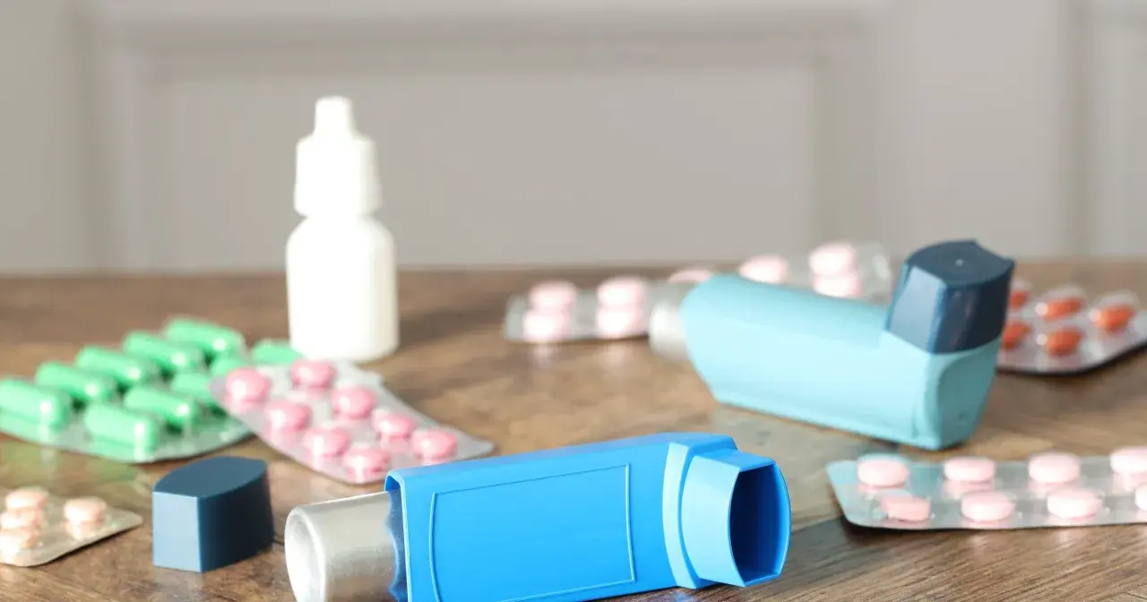 Dwa niebieskie inhalatory i opakowania leków, w tym zielone kapsułki i różowe tabletki. To zestaw na astmę, czyli oxodil combo.