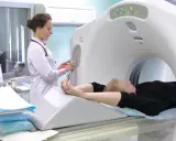 Pacjent leży na stole tomografu komputerowego, a technik przygotowuje badanie. Wynik tomografii komputerowej będzie kluczowy dla dalszego leczenia.