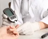Lekarz mierzy poziom cukru 99 na czczo. Na stole leży glukometr, nakłuwacz i pojemnik z paskami testowymi.