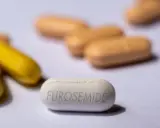 Biała tabletka z napisem FUROSEMIDE na pierwszym planie, otoczona innymi tabletkami w kolorze żółtym i beżowym.