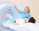 Pacjentka leży na stole do rezonansu magnetycznego. Technik obsługuje panel sterowania, przygotowując badanie rezonans magnetyczny kręgosłupa piersiowego.