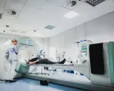 Pacjent leży na stole aparatu do tomografii komputerowej, nadzorowany przez technika.