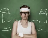 Chudy mężczyzna w okularach i opasce na głowie, z narysowanymi po bokach bicepsami, jakby po zażyciu omnadren 250.