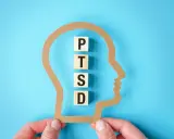 Klocki z literami P, T, S, D układają się w napis PTSD wewnątrz sylwetki głowy. Symbolizuje to wpływ zespołu stresu pourazowego, znanego w ICD-10.
