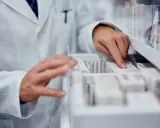 Farmaceuta szuka zamiennika leku Zarixa, przeglądając opakowania leków w aptece.