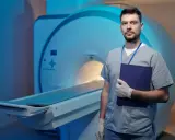 Lekarz w rękawiczkach z teczką stoi obok aparatu MRI. Dyskutuje o powikłaniach po rezonansie magnetycznym bez kontrastu.