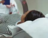 Kobieta leży na stole do rezonansu magnetycznego. Czy na rezonans magnetyczny można mieć hybrydy? Lekarz w białym fartuchu obserwuje badanie.