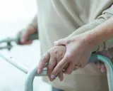 Dłonie starszej osoby i opiekuna na ramie chodzika, wsparcie przy problemach z poruszaniem się, które mogą być związane z zaburzeniami chodu ICD10.