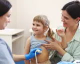 Lekarz wykonuje usg brzuszka niemowlaka. Uśmiechnięta dziewczynka i jej mama towarzyszą badaniu.