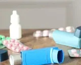 Dwa niebieskie inhalatory i opakowania leków, w tym zielone kapsułki i różowe tabletki. To zestaw na astmę, czyli oxodil combo.