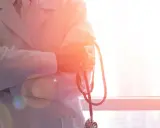 Lekarz w białym kitlu trzyma stetoskop. W tle okno z widokiem na miasto. To symbol najlepszych hematologów w Polsce.