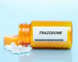 Pomarańczowa butelka z tabletkami trazodone neuraxpharm, kilka tabletek rozsypanych obok.