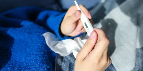 Dłonie trzymające termometr, chusteczki i niebieski sweter. Może to być objaw choroby, np. liszajec ICD-10.