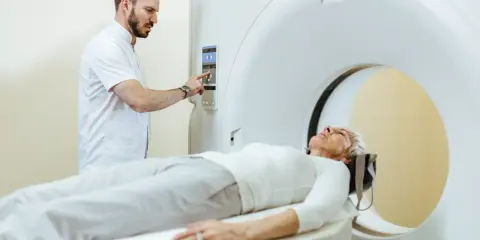 Pacjentka leży na łóżku aparatu do rezonansu magnetycznego, a technik przygotowuje badanie. Czy do rezonansu magnetycznego trzeba się rozebrać? Zazwyczaj tak, aby zdjąć metalowe przedmioty.