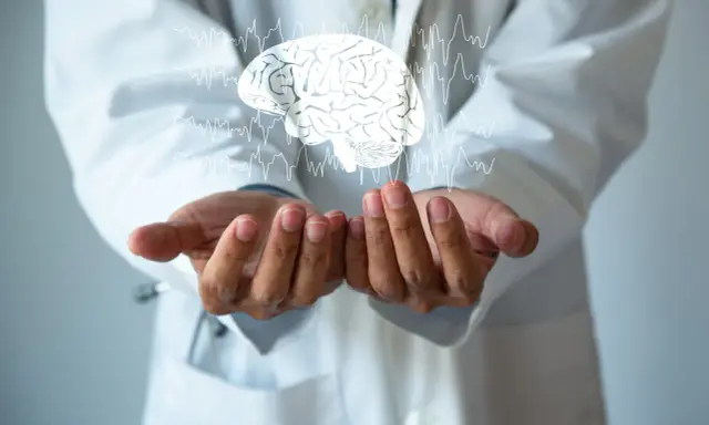 Dłonie lekarza w białym kitlu unoszą cyfrowy mózg z liniami EKG. Może to symbolizować diagnozę i leczenie chorób neurologicznych, np. i69 kod choroby.