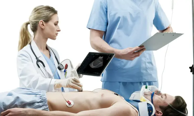 Lekarka wykonuje USG pacjenta, który leży na stole. Obok stoi lekarz z notatkami. Szybka diagnostyka to klucz do ratowania życia.
