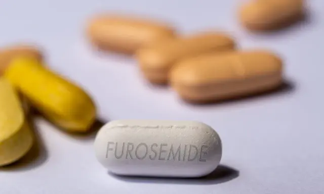 Biała tabletka z napisem FUROSEMIDE na pierwszym planie, otoczona innymi tabletkami w kolorze żółtym i beżowym.