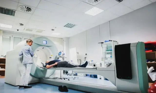 Pacjent leży na stole aparatu do tomografii komputerowej, nadzorowany przez technika.