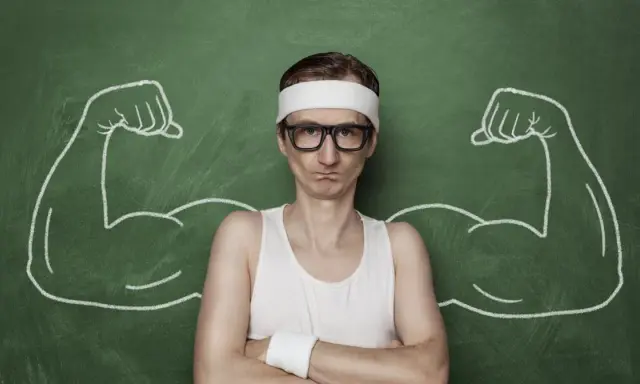 Chudy mężczyzna w okularach i opasce na głowie, z narysowanymi po bokach bicepsami, jakby po zażyciu omnadren 250.