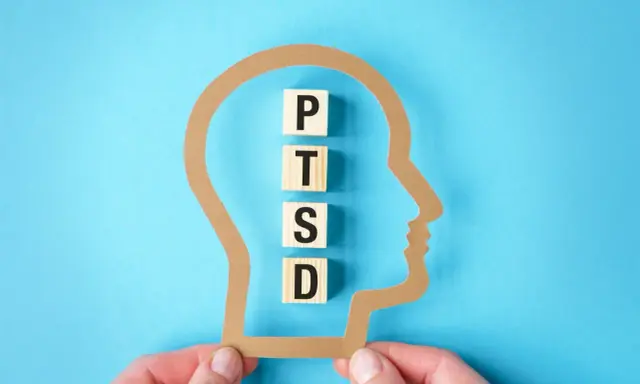 Klocki z literami P, T, S, D układają się w napis PTSD wewnątrz sylwetki głowy. Symbolizuje to wpływ zespołu stresu pourazowego, znanego w ICD-10.