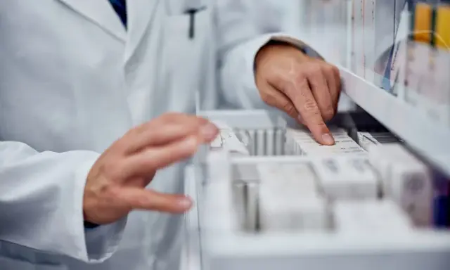 Farmaceuta szuka zamiennika leku Zarixa, przeglądając opakowania leków w aptece.