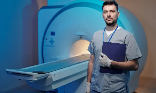 Lekarz w rękawiczkach z teczką stoi obok aparatu MRI. Dyskutuje o powikłaniach po rezonansie magnetycznym bez kontrastu.