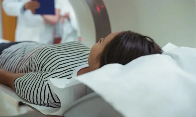 Kobieta leży na stole do rezonansu magnetycznego. Czy na rezonans magnetyczny można mieć hybrydy? Lekarz w białym fartuchu obserwuje badanie.