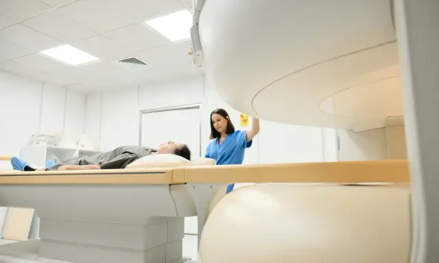 Pacjent leży na stole do rezonansu magnetycznego, pielęgniarka przygotowuje badanie. Rezonans barku interpretacja jest kluczowa dla diagnozy.
