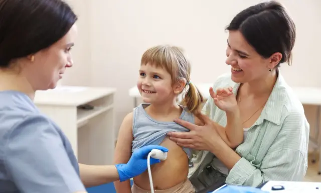 Lekarz wykonuje usg brzuszka niemowlaka. Uśmiechnięta dziewczynka i jej mama towarzyszą badaniu.