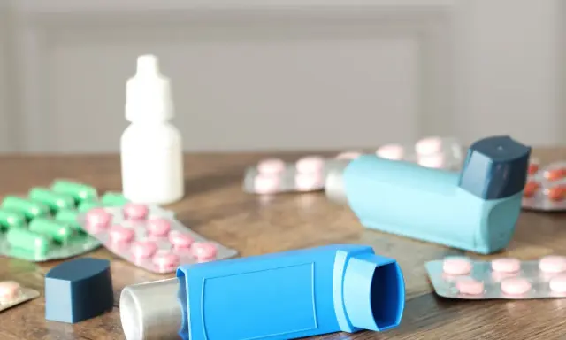 Dwa niebieskie inhalatory i opakowania leków, w tym zielone kapsułki i różowe tabletki. To zestaw na astmę, czyli oxodil combo.