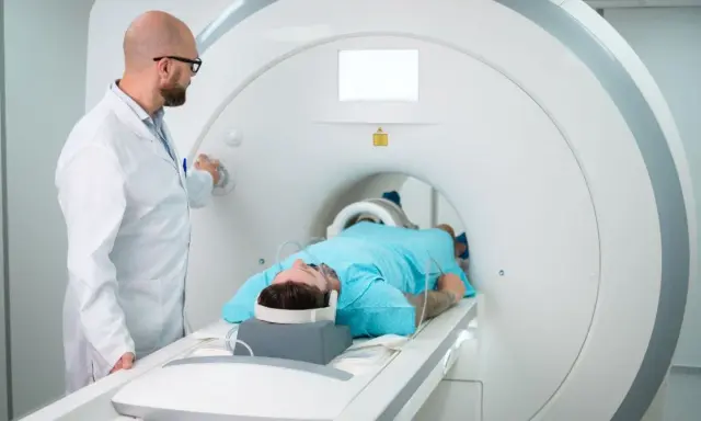 Lekarz nadzoruje badanie rezonansem kolana pacjenta leżącego w aparacie MRI.
