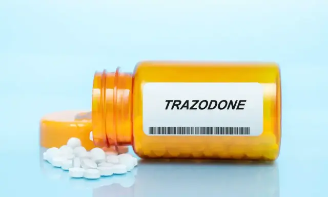 Pomarańczowa butelka z tabletkami trazodone neuraxpharm, kilka tabletek rozsypanych obok.