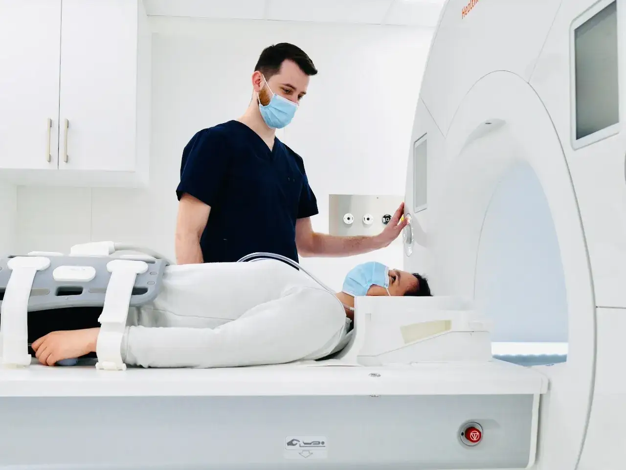 Pacjentka leży w aparacie MRI, gdzie rezonans całego organizmu wykrywa szczegółowe obrazy. Technik w masce nadzoruje badanie.