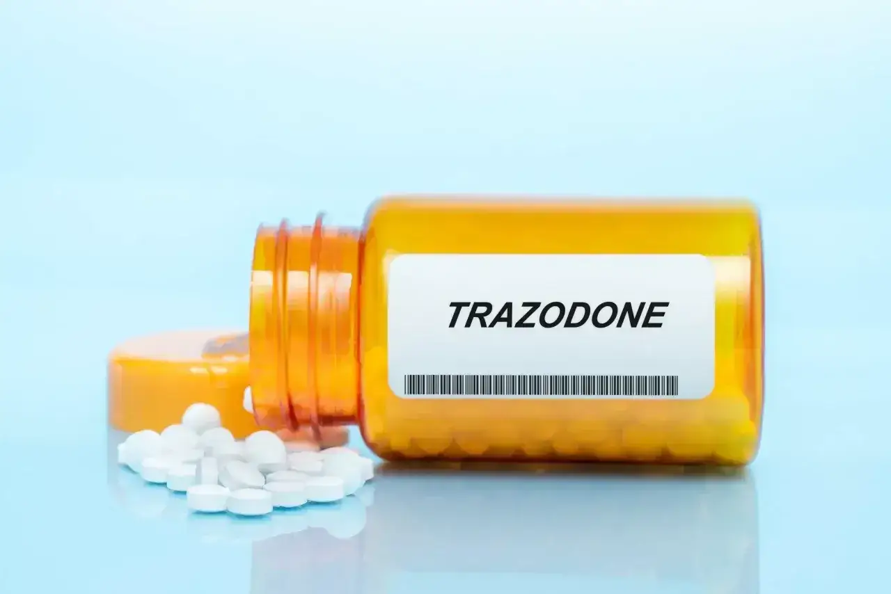 Pomarańczowa butelka leku trazodone neuraxpharm z rozsypanymi tabletkami.
