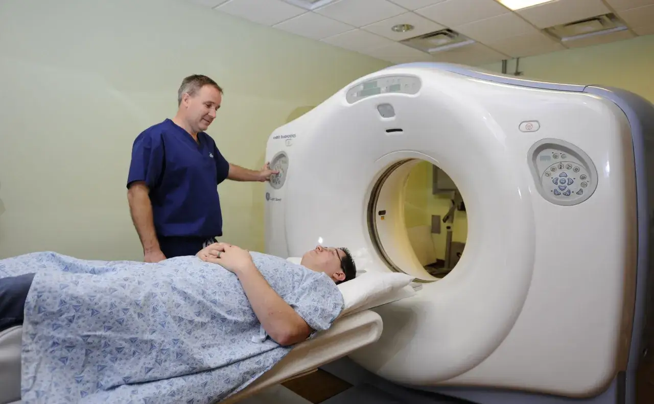 Pacjent leży na stole tomografu, a technik przygotowuje badanie. Czy na tomografię trzeba być na czczo? Zależy od zaleceń lekarza.