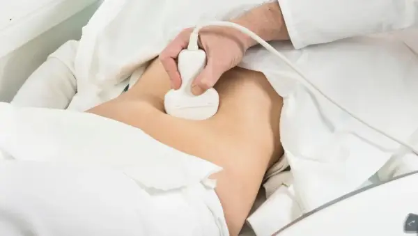 Lekarz wykonuje badanie usg prostaty. Pacjent leży pod białym obrusem, a sonda aparatu USG jest przykładana do brzucha.